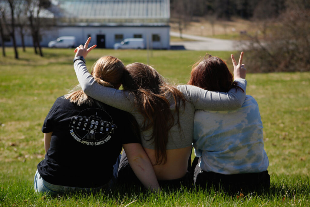 Kuva jossa opisklejat istuvta nurmikolla ja ovta yhdessä kuvaaja Alicia Fredekrion
